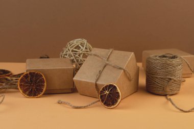 Noel hediyesi kutuları, sarmaşık topları ve pastel kum rengi arka planda kuru portakal dilimleri..