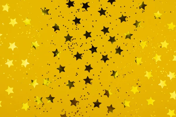 Estrelas douradas no fundo amarelo. Plástico estrelas brilhantes como fundo brilhante. Fundo de Natal, Ano Novo. Deitado plano, vista superior . — Fotografia de Stock
