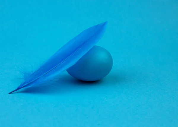 Пасхальные разноцветные яйца и перья на синем фоне . — стоковое фото
