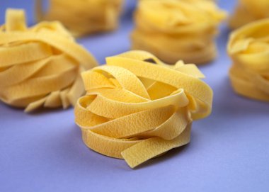 Pişmemiş geleneksel İtalyan makarnası menekşe arka planda. Çiğ fettucine, tagliatelle veya pappardelle porsiyonu.