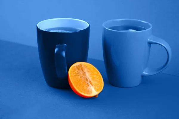 青の古典的な背景にホットティーとオレンジの半分の2杯. — ストック写真