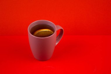 Bir fincan sıcak çay ve turuncu arka planda yarım portakal..