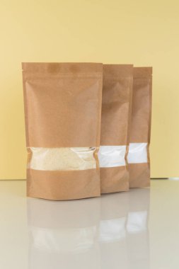 Kahverengi kraft kağıdından çanta ve sarı arka planda erzak. Gıda ve mallar için ambalaj tasarımı. Ağırlık ürünleri için pencereli paketler.