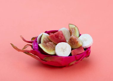 Meyve karışımının içinde yarı ejderha meyvesi ya da pitaya. Dilimlenmiş incir, muz ve guava. Turuncu arka planda..