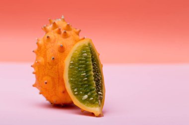 Bir portakallı Kiwano ve yarım Kinavo pembe ve turuncu arka planda egzotik meyveler yiyor. Boynuzlu kavun.