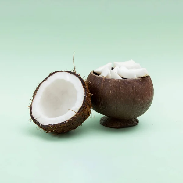 Half of coconut and coconut pieces in wooden vase on mint background. Front view.