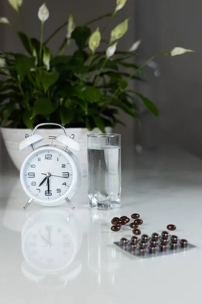 Vit Väckarklocka Och Medicinska Piller Med Ett Glas Vatten Bordet — Stockfoto