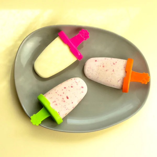 Keto ice cream sticks with strawberries without sugar. Sweetener erythritol. Light yellow background.
