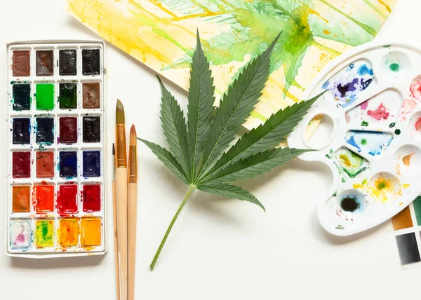 Uppsättning akvarellfärger, konstborstar, palett och blankt album. Marijuanablad. Cannabis avslöjar kreativitet. Begreppet konst. — Stockfoto