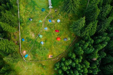 Camping site with tents seen from a drone in the dense woods.