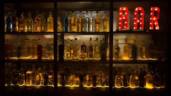 BAR sign with lights in the dark with bottles of alcohol.