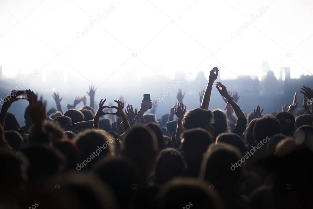 Stage lights and crowd of audience with hands raised at a music festival. Fans enjoying the party vibes.