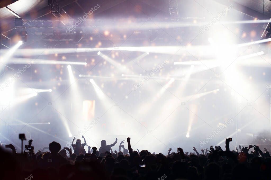 Stage lights and crowd of audience with hands raised at a music festival. Fans enjoying the party vibes.