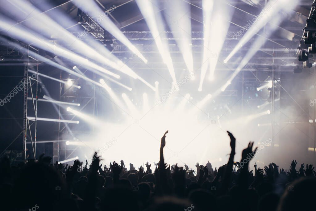 Stage lights and crowd of audience with hands raised at a music festival. Fans enjoying the party vibes.