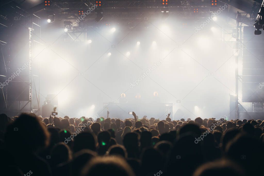 Stage lights and crowd of audience with hands raised at a music festival. Fans enjoying the party vibes.