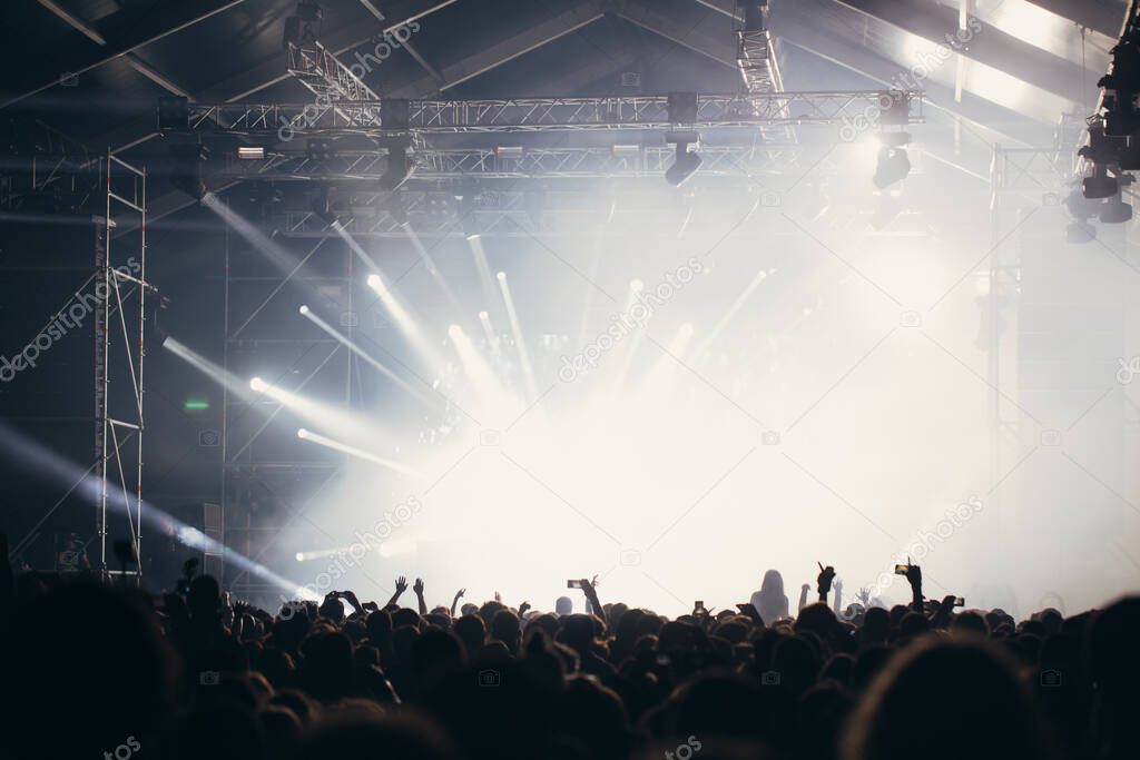 Stage lights and crowd of audience with hands raised at a music festival. Fans enjoying the party vibes.