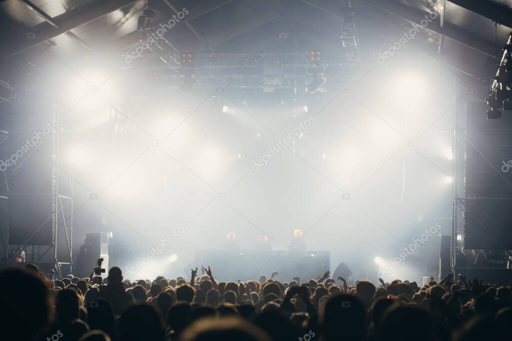 Stage lights and crowd of audience with hands raised at a music festival. Fans enjoying the party vibes.