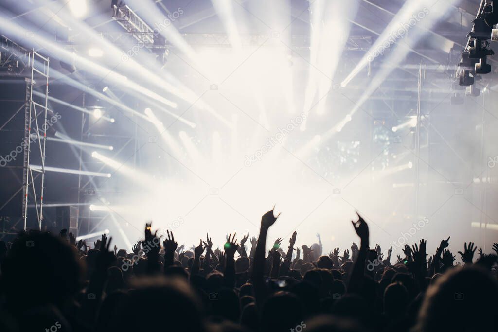 Stage lights and crowd of audience with hands raised at a music festival. Fans enjoying the party vibes.