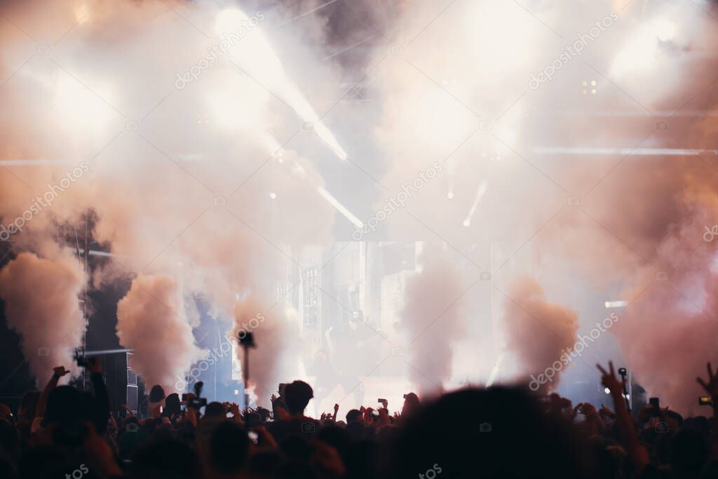 Stage lights and crowd of audience with hands raised at a music festival. Fans enjoying the party vibes.