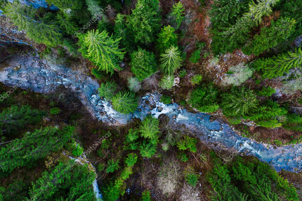 Creek winding through cliffs and forests seen from a drone