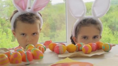 Kafasında tavşan kulağı olan komik çocuk ve kız. Mutlu Paskalyalar için giyinmiş çocuklar. Pencerenin arkasında paskalya yumurtası olan çocuklar..