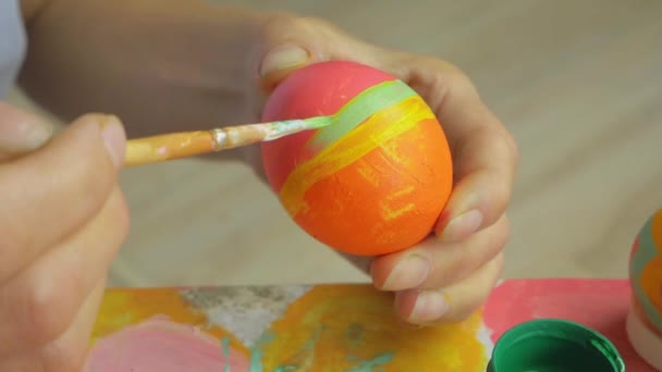 Ένα κορίτσι ζωγραφίζει ένα ριγέ μοτίβο σε ένα πασχαλινό αυγό. Το χέρι κρατά μια βούρτσα σε φόντο πασχαλινών αυγών. Πάσχα διακόσμηση προετοιμασία ευτυχισμένο Πάσχα — Αρχείο Βίντεο