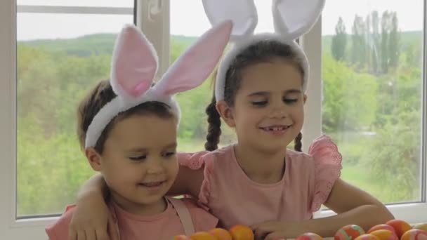 Engraçado menino e menina com orelhas de coelho na cabeça. Crianças vestidas para a Feliz Páscoa. Crianças com ovos de Páscoa no fundo da janela . — Vídeo de Stock