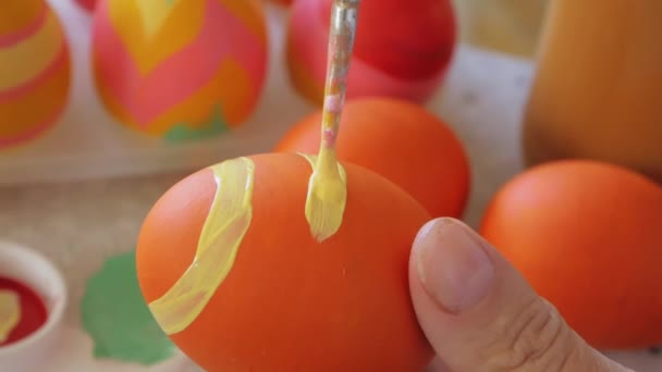 A menina desenha um padrão listrado em um ovo de Páscoa. A mão mantém uma escova em um contexto de ovos de Easter. Decoração de Páscoa preparar páscoa feliz — Vídeo de Stock