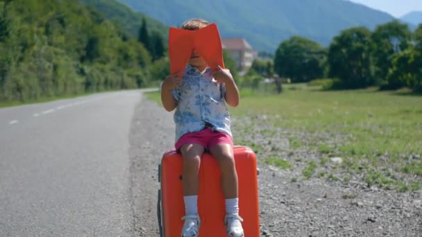 Mignon tout-petit garçon avec valise et palmes s'amuse à attendre le voyage et agitant ses palmes dans l'air frais le long de la route. Loisirs, week-end, voyage et tourisme concept — Video