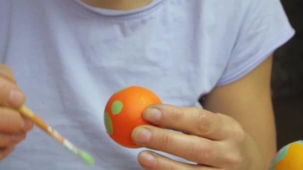 De hand schildert een paasei met een borstel en zet op een standaard. Het meisje tekent een streepjespatroon op een ei. Paasversiering, voorbereiding op gelukkig Pasen — Stockvideo