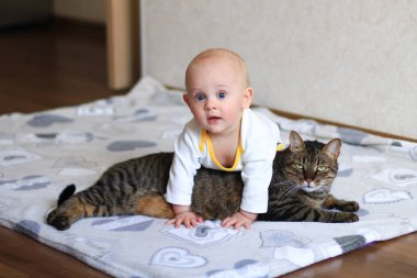 Yerde sürünen bebek ve tekir bir kedi.