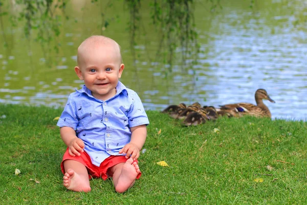 Lindo Sonriente Niño Feliz Sentado Hierba Parque Con Lago Patos —  Fotos de Stock