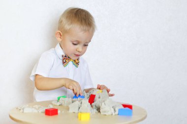 Şirin sarışın çocuk kinetik kumla oynuyor, küçük çocuklarda iyi motor becerileri geliştirmek için harika bir eğitim aktivitesi.