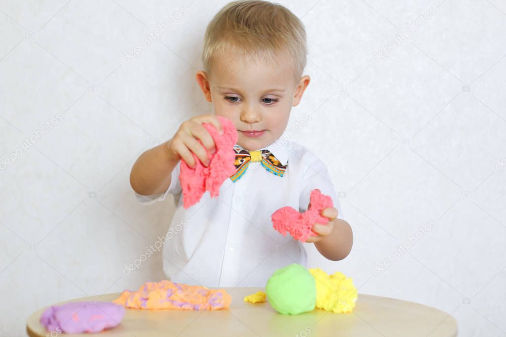 2 year old toddler boy is playing with kinetic modeling clay, plasticine, play-dough, a fun activity to develop fine motor skills in young children 