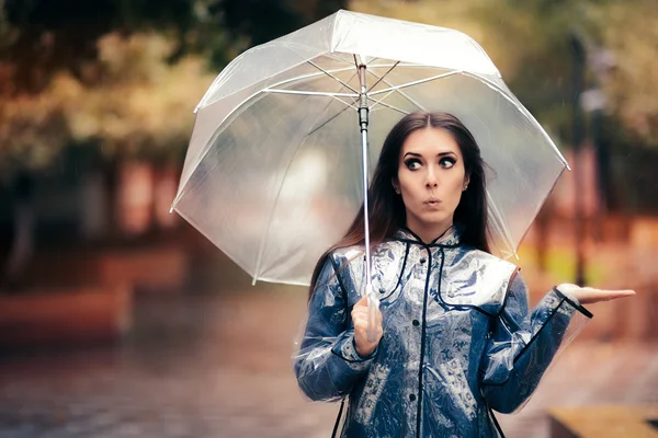 Mulher com capa de chuva transparente e guarda-chuva verificando a chuva — Fotografia de Stock