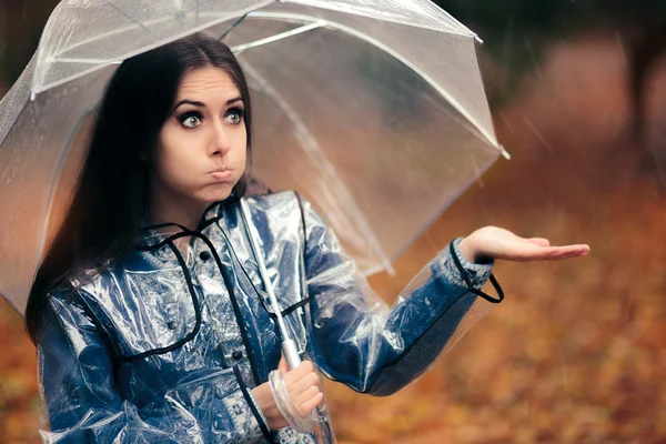 Mulher com capa de chuva transparente e guarda-chuva verificando a chuva — Fotografia de Stock