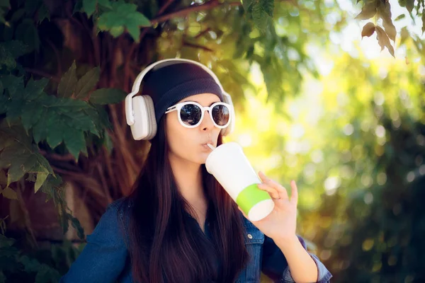 Холодная девушка в джинсах, пьющая сок и слушающая музыку — стоковое фото