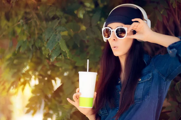 Funny Girl in Jeans Outfit Mengenakan kacamata hitam Minum Juice dan mendengarkan musik — Stok Foto