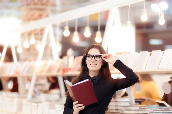 Sorrindo menina segurando um livro na frente de uma estante — Fotografia de Stock