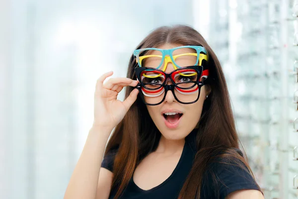 Mujer divertida probando muchos marcos de gafas en la tienda óptica — Foto de Stock