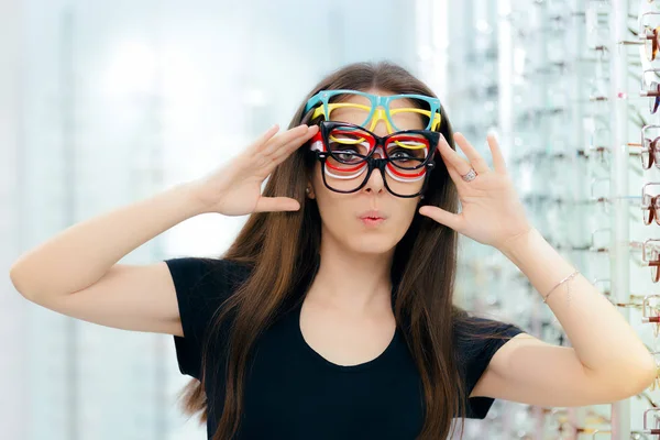 Mulher engraçada tentando muitos quadros de óculos na loja óptica — Fotografia de Stock