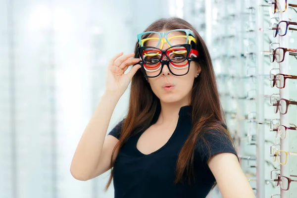 Mulher engraçada tentando muitos quadros de óculos na loja óptica — Fotografia de Stock