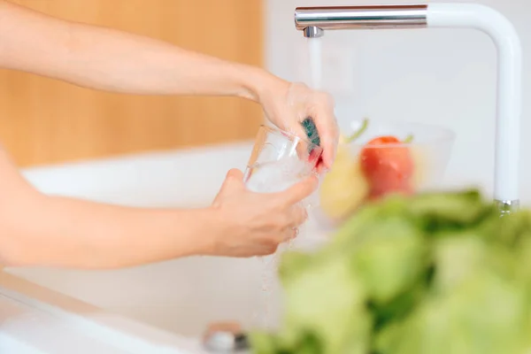Person Washing a Glass in Kitchen Sink