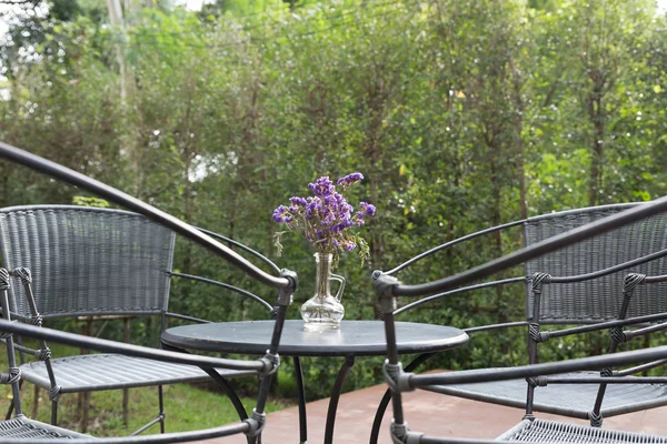 Flor púrpura en jarrón de vidrio, silla de mimbre en el patio — Foto de Stock