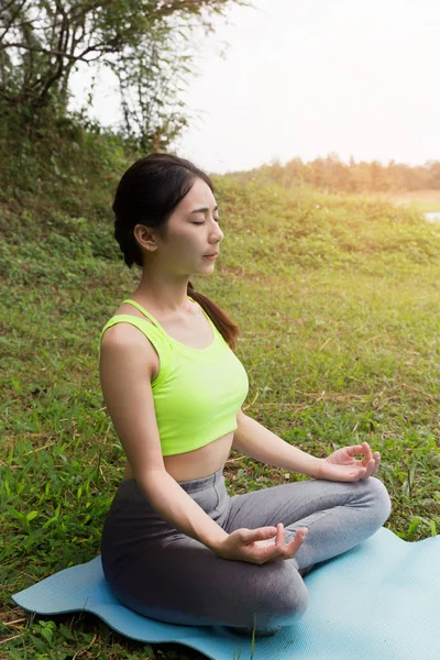 Junge Frau meditiert während sie Yoga im Freien im Park praktiziert, — Stockfoto