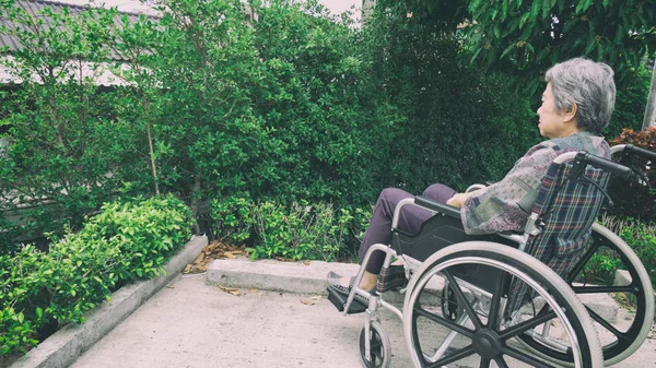 Old woman sitting alone in a wheelchair out in the garden.