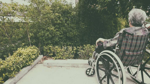 Gammal kvinna sitter ensam i en rullstol ute i trädgården. — Stockfoto