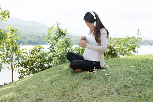 Jovem mulher asiática sentada na grama fresca primavera ouvindo mus — Fotografia de Stock