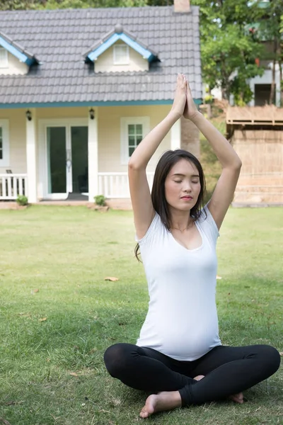Asiatische schwangere Frau praktiziert Yoga auf grünem Gras vor — Stockfoto