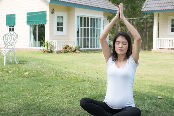 Asiatische schwangere Frau praktiziert Yoga auf grünem Gras vor — Stockfoto